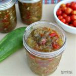 several jars filled with food sitting on top of a table next to a bowl of tomatoes