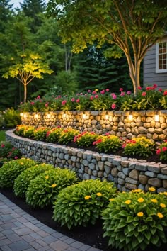 a stone wall with flowers and lights in the middle of it at night, surrounded by greenery