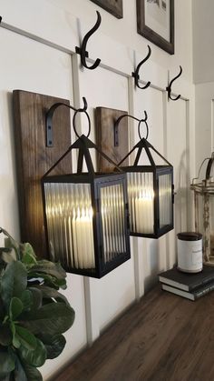 two lanterns are hanging on the wall next to a potted plant and some books