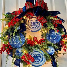 a blue and white christmas wreath with red berries, pine cones and evergreens hanging from the front door