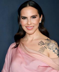 a woman in a pink dress with tattoos on her arm and shoulder, smiling at the camera