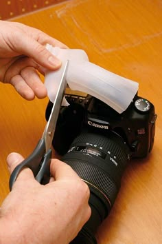 a person cutting something with a pair of scissors on top of a wooden table next to a camera