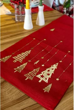 a red table runner with gold christmas trees on it and candles in vases next to it