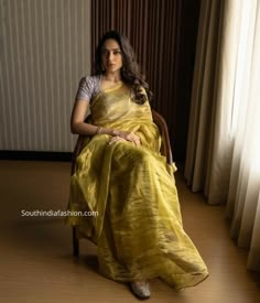 a woman in a yellow sari sitting on a chair with her legs crossed and looking off to the side