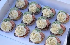 twelve cupcakes with white frosting and pink flowers in a box on a table