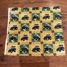 a quilted table runner with cars on yellow and green squares in the center, sitting on a wooden floor