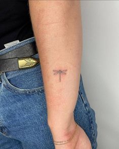 a woman's arm with a small dragonfly tattoo on it