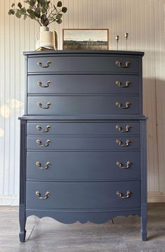 a blue chest of drawers with gold handles and knobs on the bottom, in front of a white wall