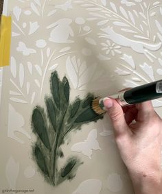 a person is painting a wall with green leaves on it and using a paint brush