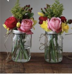 two mason jars filled with flowers sitting on top of a wooden table next to each other