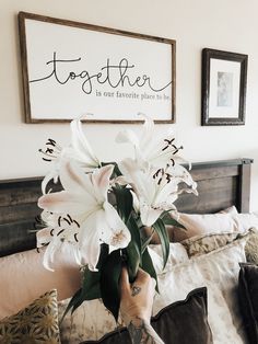 a person holding a bouquet of flowers on top of a bed in front of two framed pictures