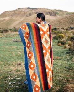 a man is wrapped up in a blanket on the side of a hill with mountains in the background