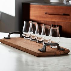 six wine glasses on a wooden tray with a black faucet in the middle