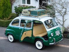 an old green and white car with luggage on it's roof rack, parked in front of a house