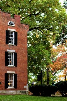 a red brick building with black shutters and trees in the back ground, on a sunny day