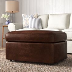 a brown ottoman sitting on top of a rug next to a white couch