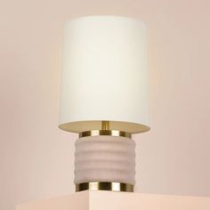 a white and gold lamp on top of a table next to a wall mounted light