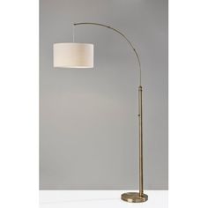 a floor lamp with a white shade on the top and a gold base, against a gray wall