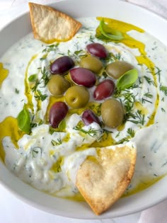 a white plate topped with olives and pita chips next to a bowl of dip