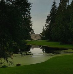 a pond in the middle of a lush green field with trees around it and a large house in the background