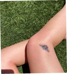 a woman's legs with a small tattoo on her left leg, laying in the grass