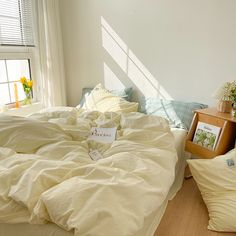 an unmade bed sitting in a bedroom next to a window with sun shining through the windows