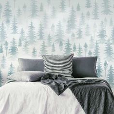 a bed with pillows and blankets in front of a wallpapered forest pattern that has pine trees on it