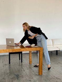 a woman leaning over a wooden table with a laptop on it