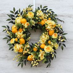 a wreath with oranges and yellow flowers hanging on a white wooden wall next to a candle