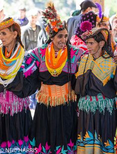 three women dressed in colorful clothing standing next to each other with people watching from the sidelines