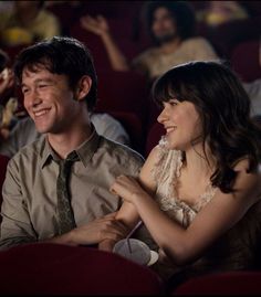 two people sitting in a movie theater, one smiling and the other looking at something