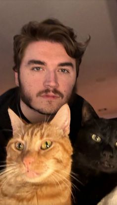 a man with two cats in front of him and one cat looking at the camera