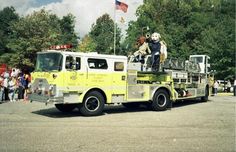 a fire truck with people standing on top of it in the parking lot next to trees