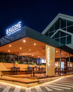 an outside view of a restaurant at night with lights on and tables in the foreground