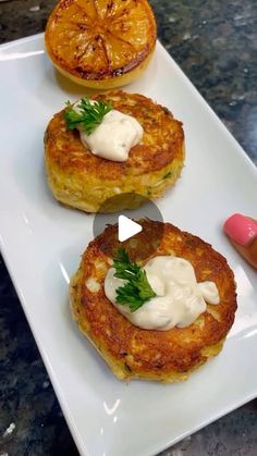 three small cakes on a white plate topped with sour cream and garnished with fresh herbs