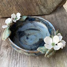 a blue bowl with white flowers sitting on top of a wooden table next to a rock