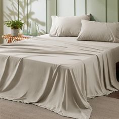 a bed covered in white sheets and pillows next to a potted plant on a table