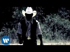 a man wearing a cowboy hat and vest walking in the grass with trees behind him