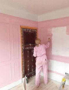 a woman in pink jumpsuit painting a wall