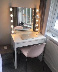 a white desk topped with a laptop computer next to a mirror and light bulbs on top of it