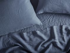 an unmade bed with blue sheets and pillows