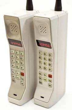 two old style telephones sitting next to each other on a white surface with red numbers