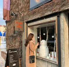 a woman looking through the window at a snowman in front of a storefront