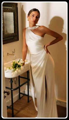 a woman standing in front of a sink wearing a white dress and holding her hand on her hip