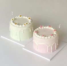 two cakes with white frosting and pink flowers on each cake stand, one is half covered in icing