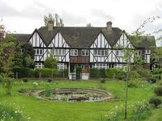 an old house with a pond in front of it and lots of greenery around the yard