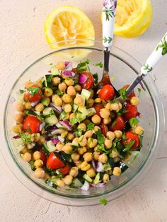 a glass bowl filled with chickpeas, lettuce and tomatoes next to a lemon wedge