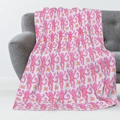 a pink blanket with monkeys on it is sitting on a gray couch next to a grey chair