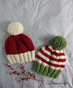 two knitted hats sitting next to each other on top of a white cloth covered surface