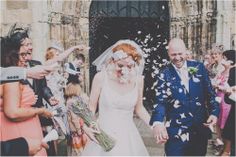 a bride and groom walking through confetti thrown from their wedding party at the church